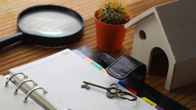 A wooden model of a house, keys and a magnifying glass